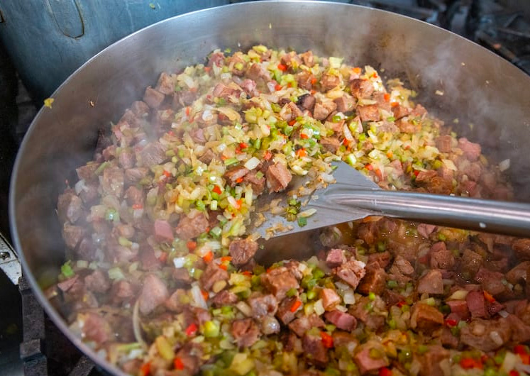 Sautéed onions, celery, and bell peppers—also known as the holy trinity—browning in a pot and  soaking up fond for jambalaya