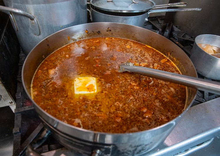 Cajun jambalaya simmering in a pot with sausage, chicken, and stock just before the rice is  added