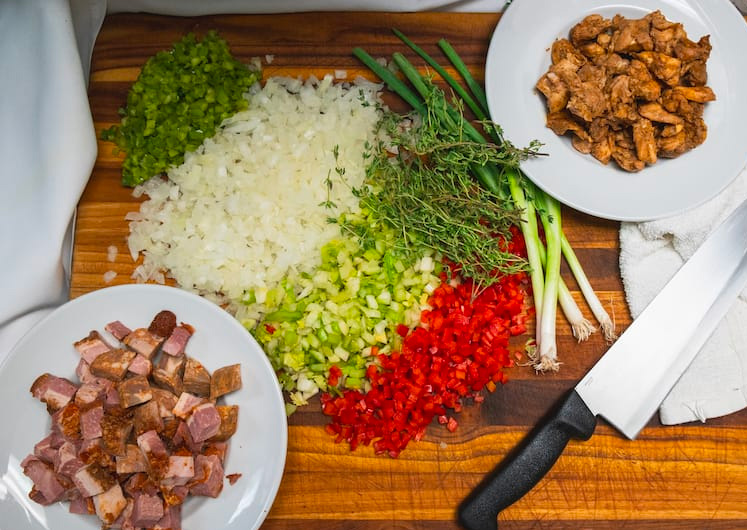 Prepped ingredients for Cajun jambalaya laid out on a kitchen counter, including  sausage, chicken, chopped vegetables, and herbs.
